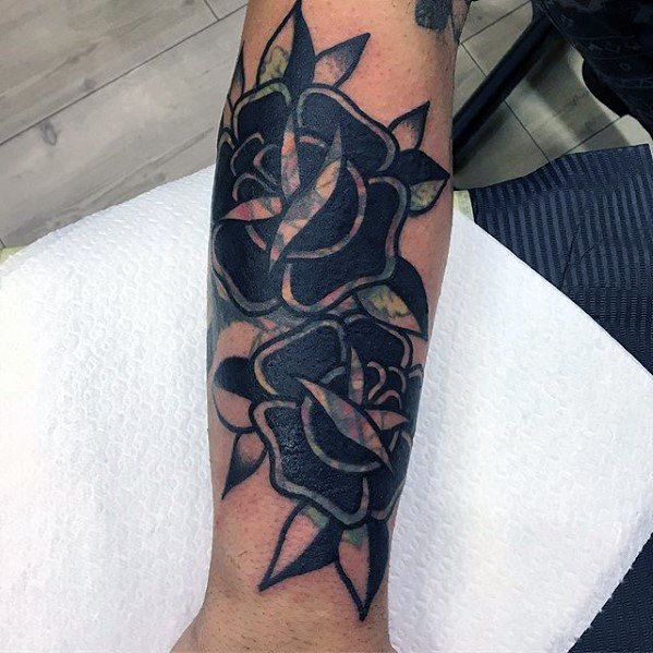 Blast over tattoo of two black roses with green leaves on a forearm against white background