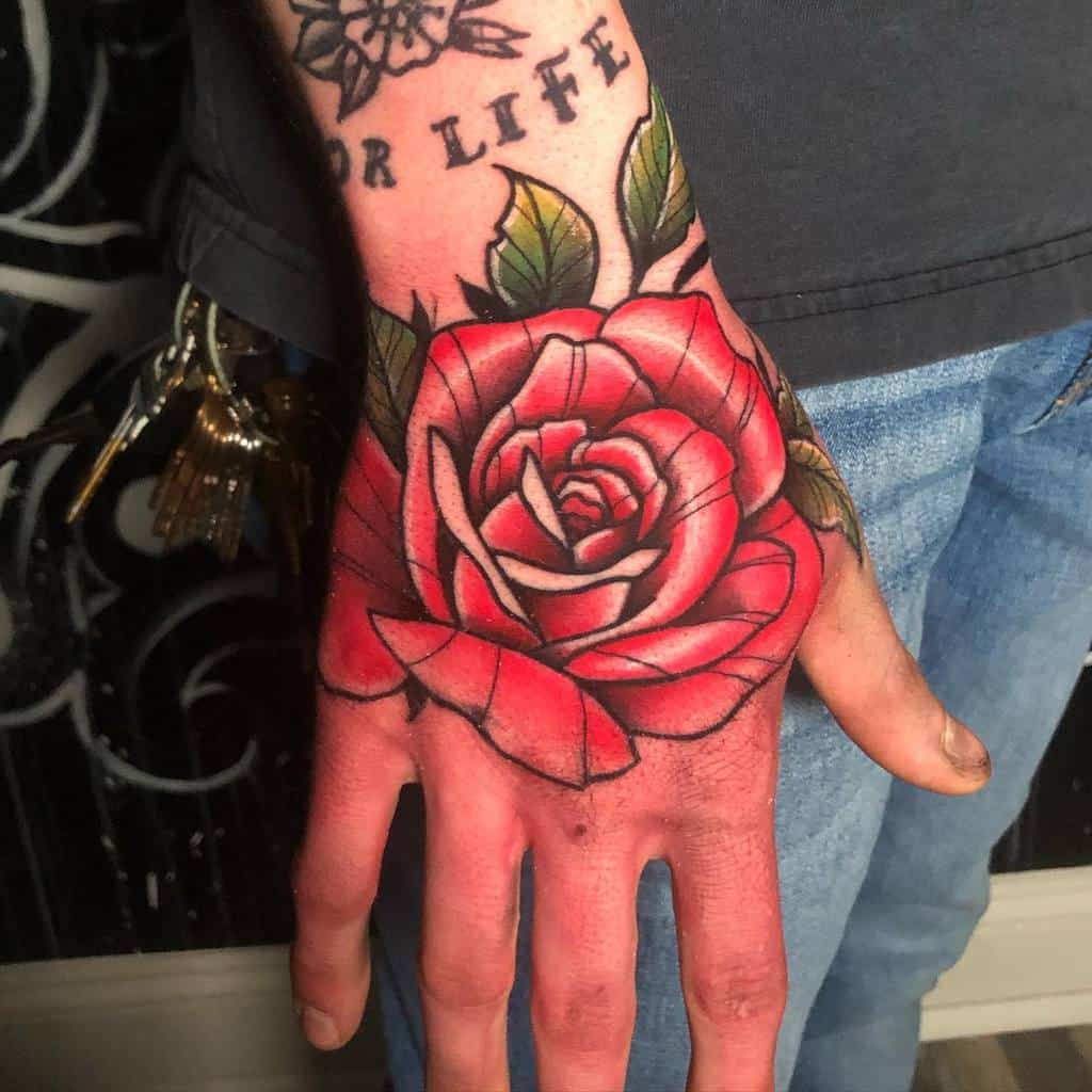 A stunning hand tattoo features a large, vibrant red rose with lush green leaves, elegantly complemented by the "FOR LIFE" text etched on the wrist