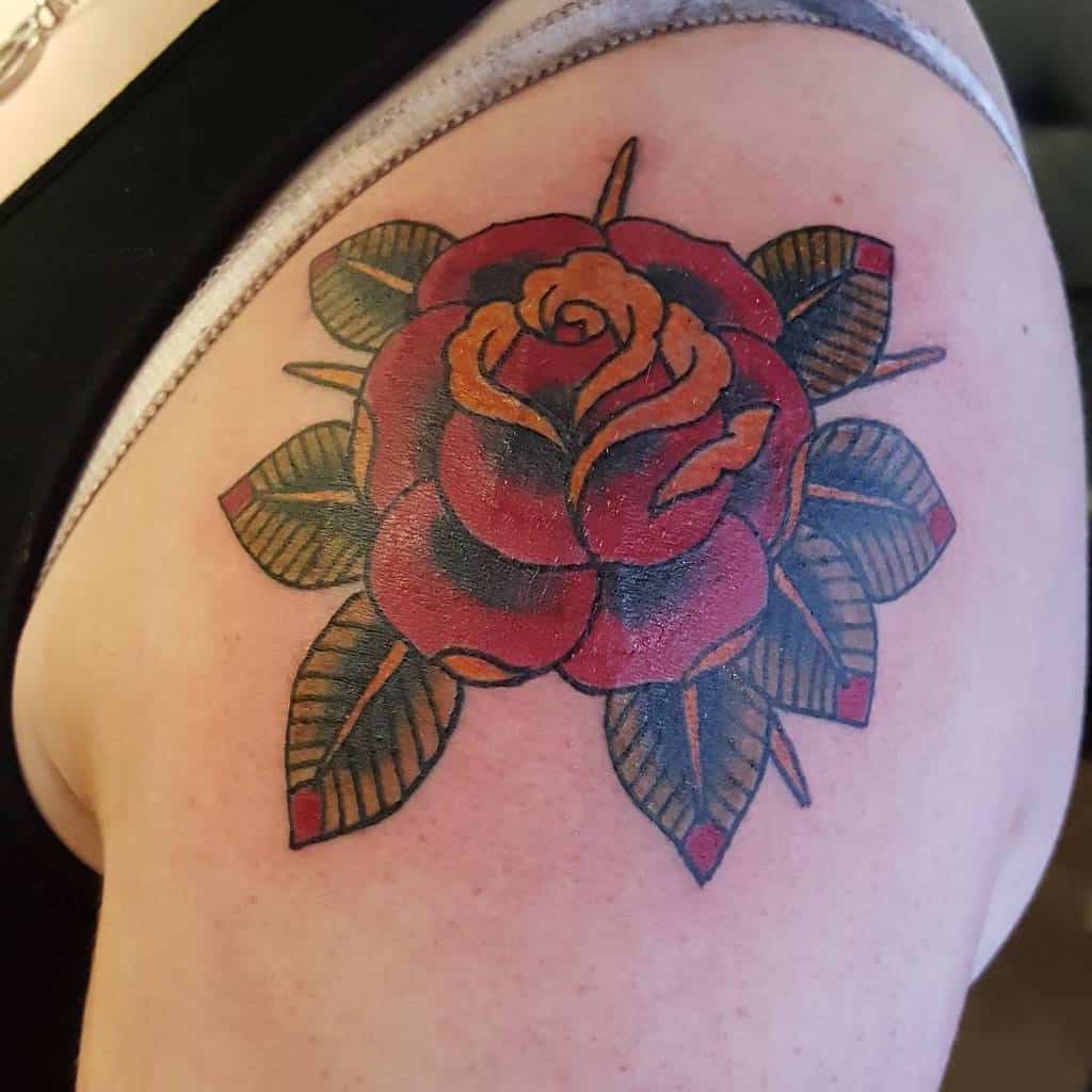 Traditional tattoo of a vibrant red rose with lush green leaves gracefully adorning the person's shoulder and upper arm