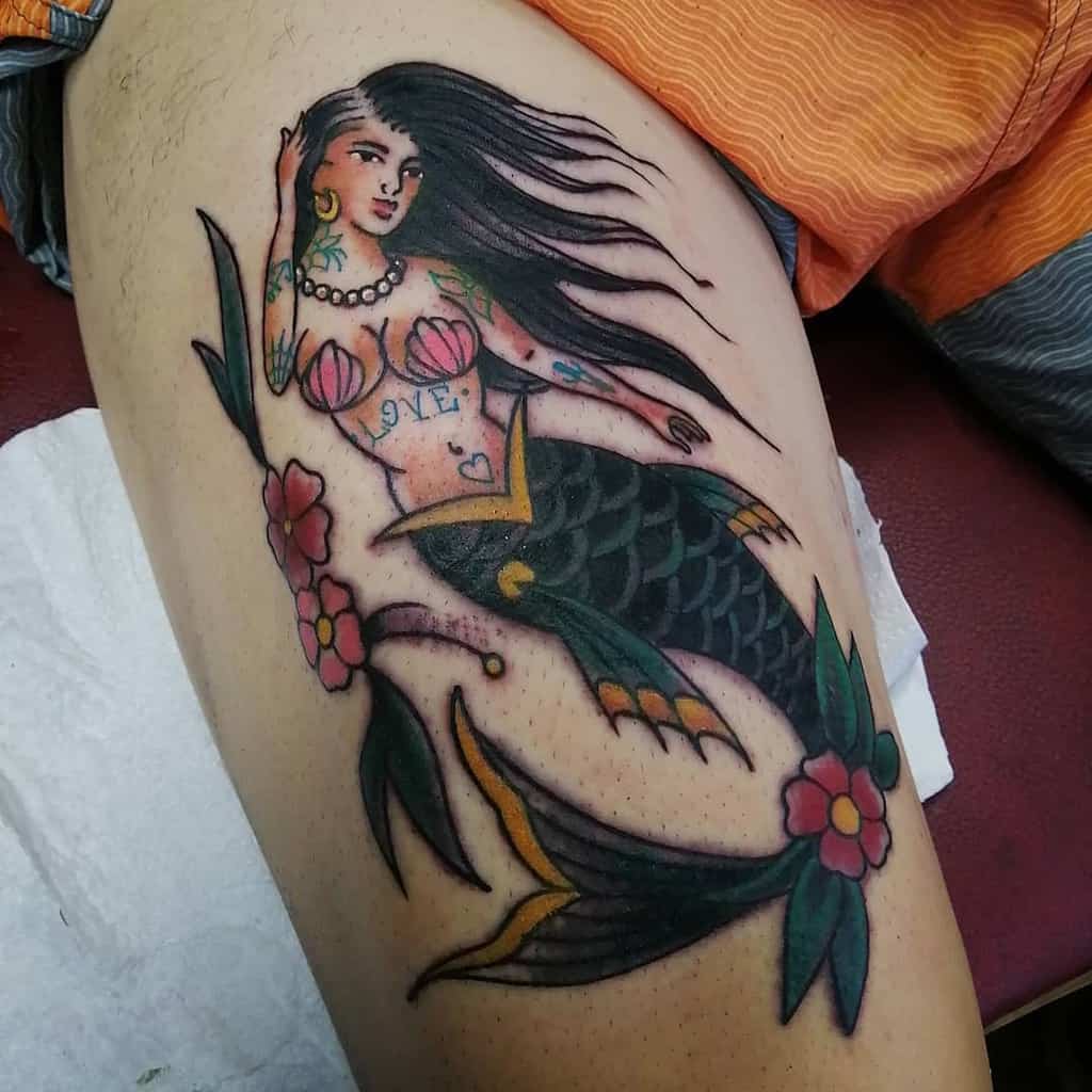 Traditional tattoo of a mermaid with flowing black hair, adorned with vibrant colors, seashell accents, floral embellishments, and charming nautical themes