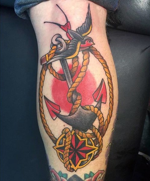 Tattoo of anchor, rope, and sparrow on a leg with a nautical star and red circle in the background