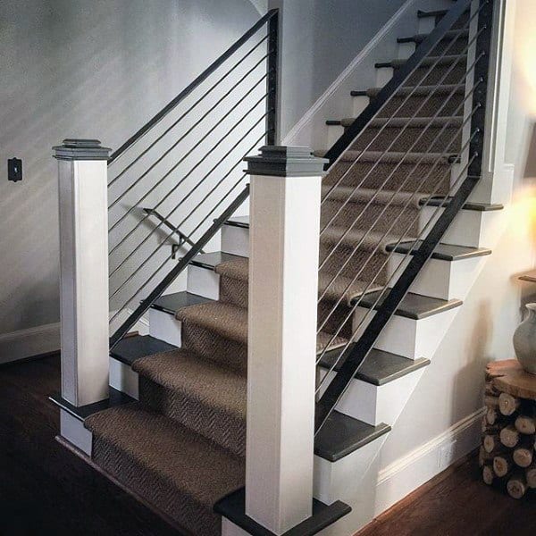 Elegant staircase with carpeted steps, metal railings, and white posts, alongside a cozy firewood stack