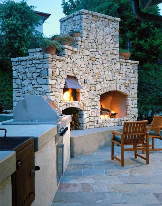 Outdoor stone fireplace with lit fire, surrounded by patio seating and a built-in grill nearby