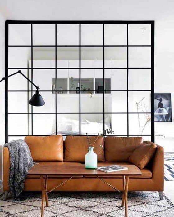 Tan leather sofa with wooden coffee table in front of a large black grid window divider.