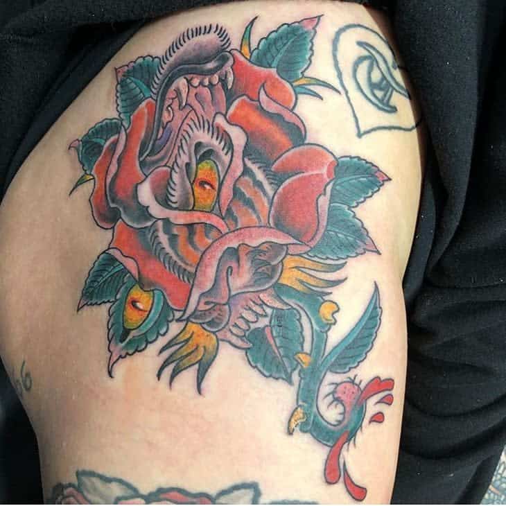 A traditional tattoo of roses with tiger-like eyes, surrounded by vibrant colors and a small bird, on the upper arm