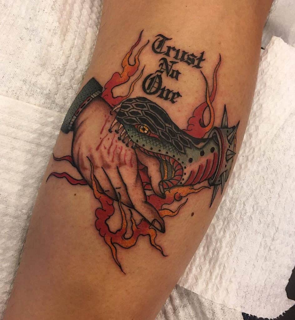 Fiery forearm tattoo with a dramatic snake handshake, paired with bold gothic text 'Trust No One,' surrounded by intense flames