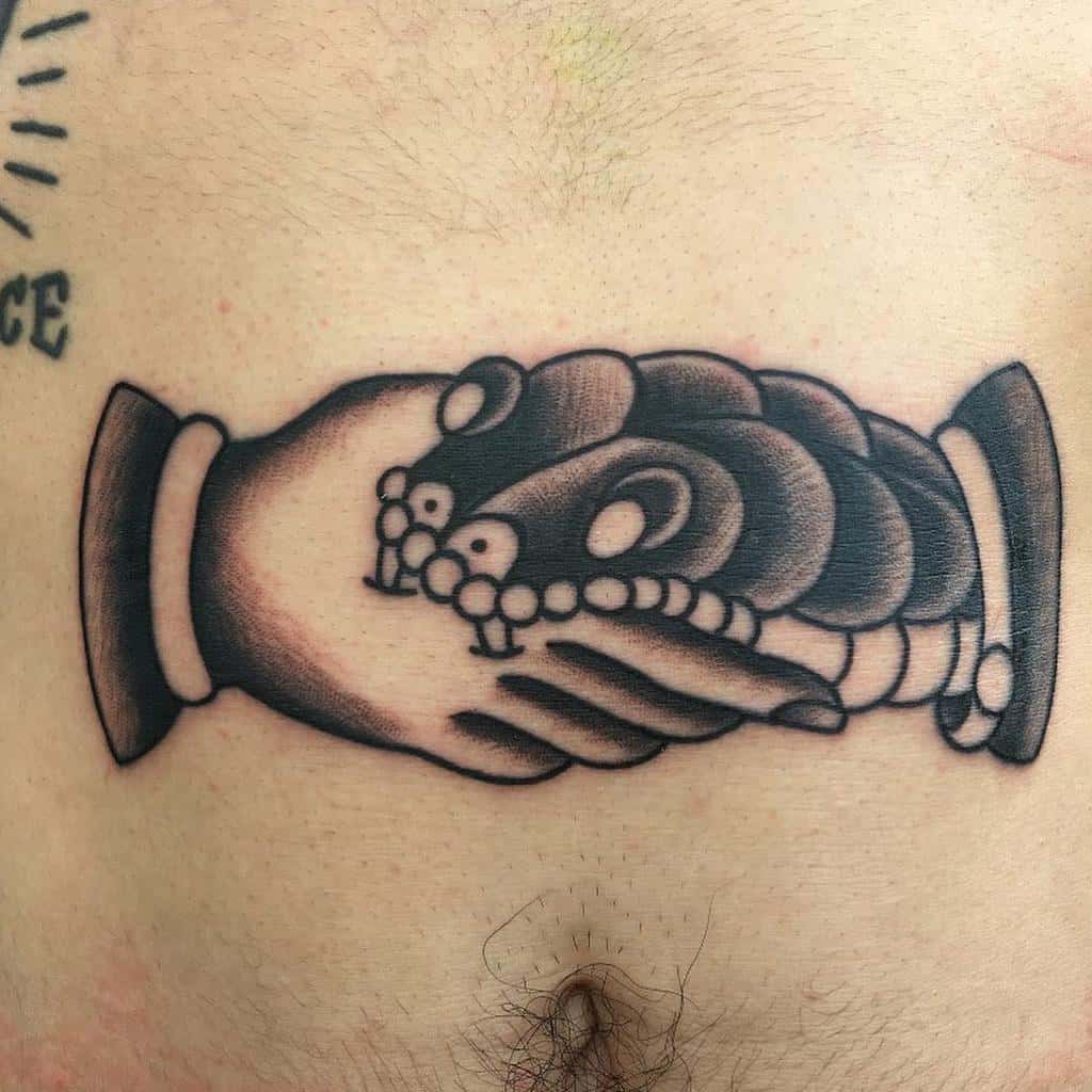 Traditional black and gray tattoo on the torso depicting a handshake between a human and a snake, symbolizing distrust