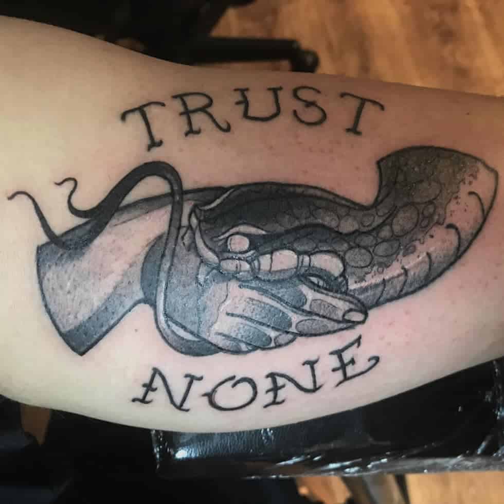 Tattoo of a handshake between a human and a snake with the words "Trust None" above and below
