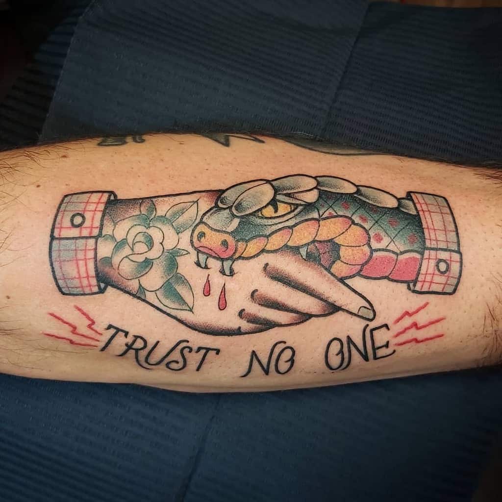 Tattoo of a snake biting a hand with a flower, with the words "TRUST NO ONE" below