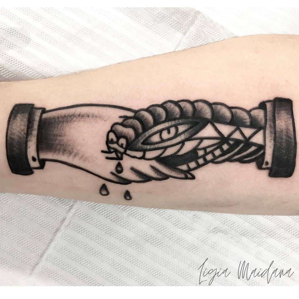 Monochrome tattoo with a detailed handshake and snake, accented with dripping drops, done in traditional blackwork style