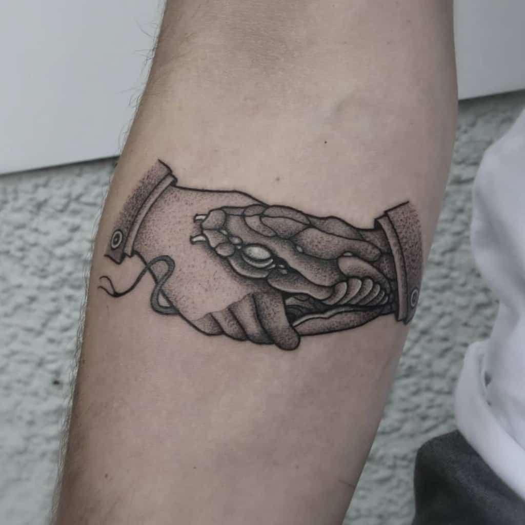 Black and gray forearm tattoo of a handshake between a human and a snake, created with detailed shading and dotwork