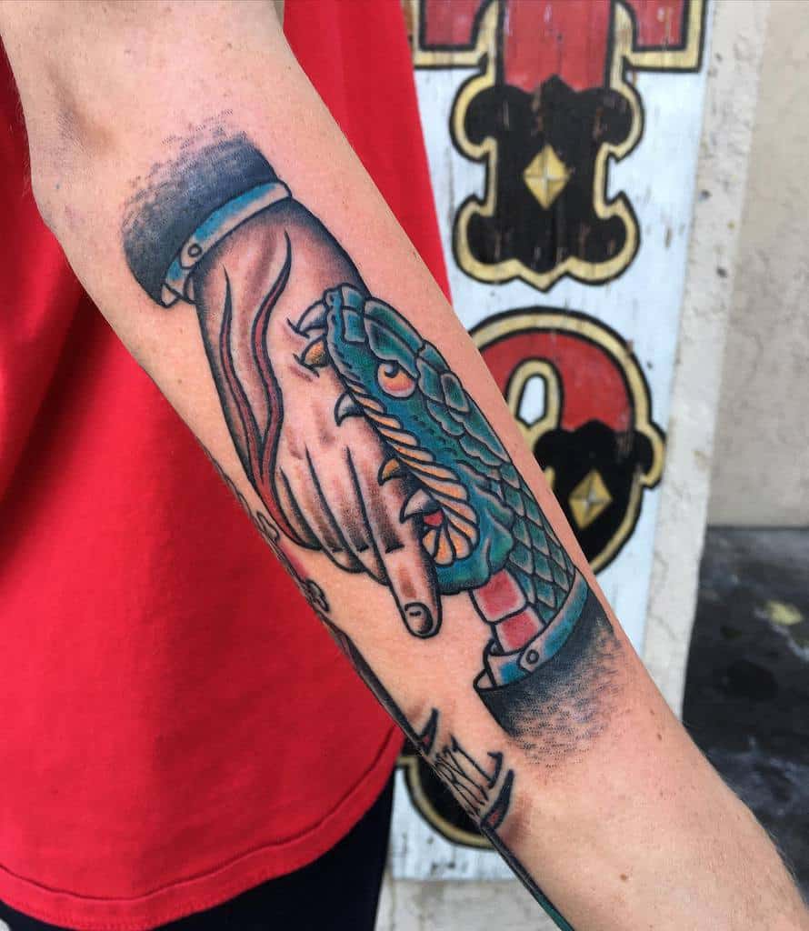 Forearm tattoo of a snake biting a hand in a handshake