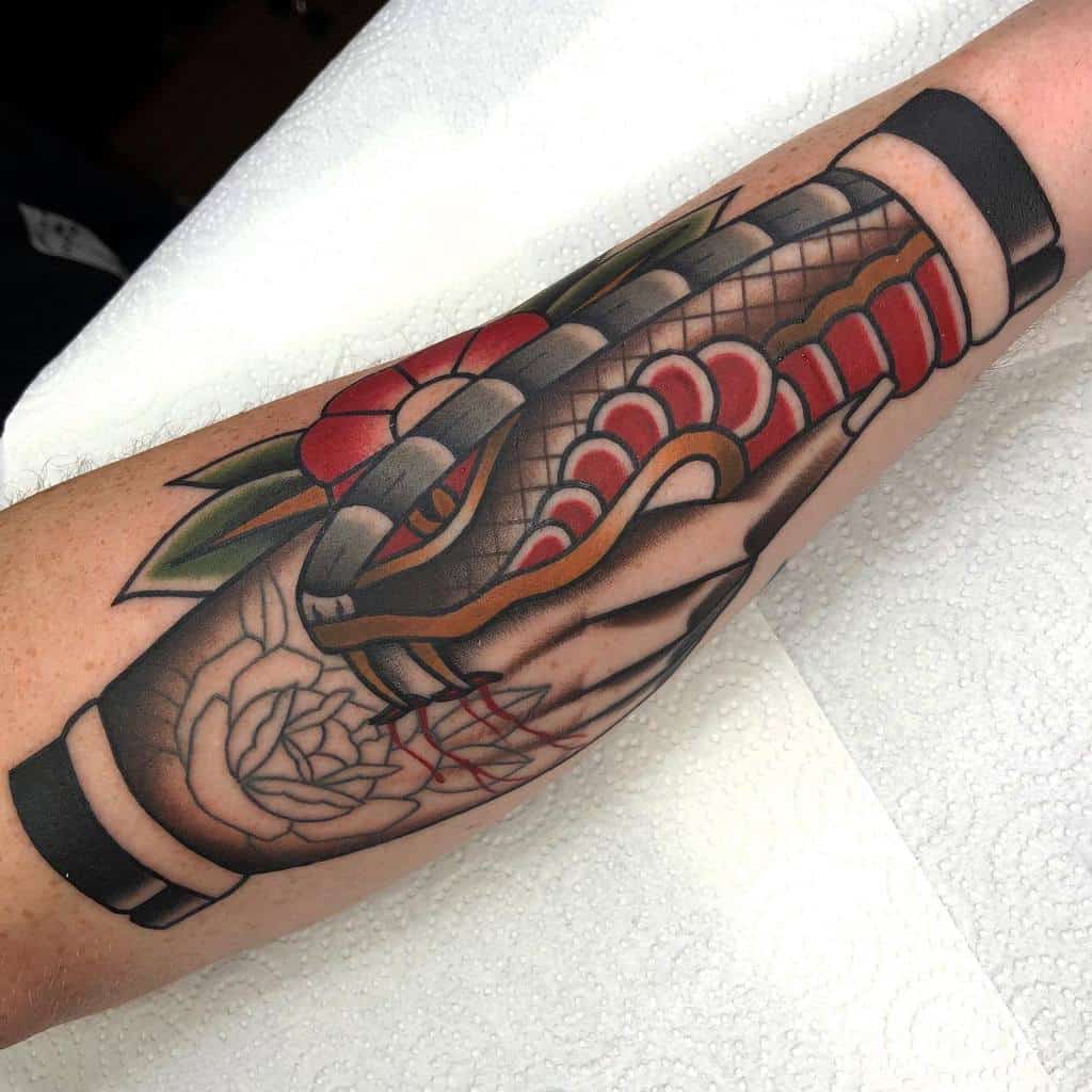 Traditional forearm tattoo showcasing a handshake with a serpent, vibrant red floral accents, and bold shading to emphasize trust and betrayal