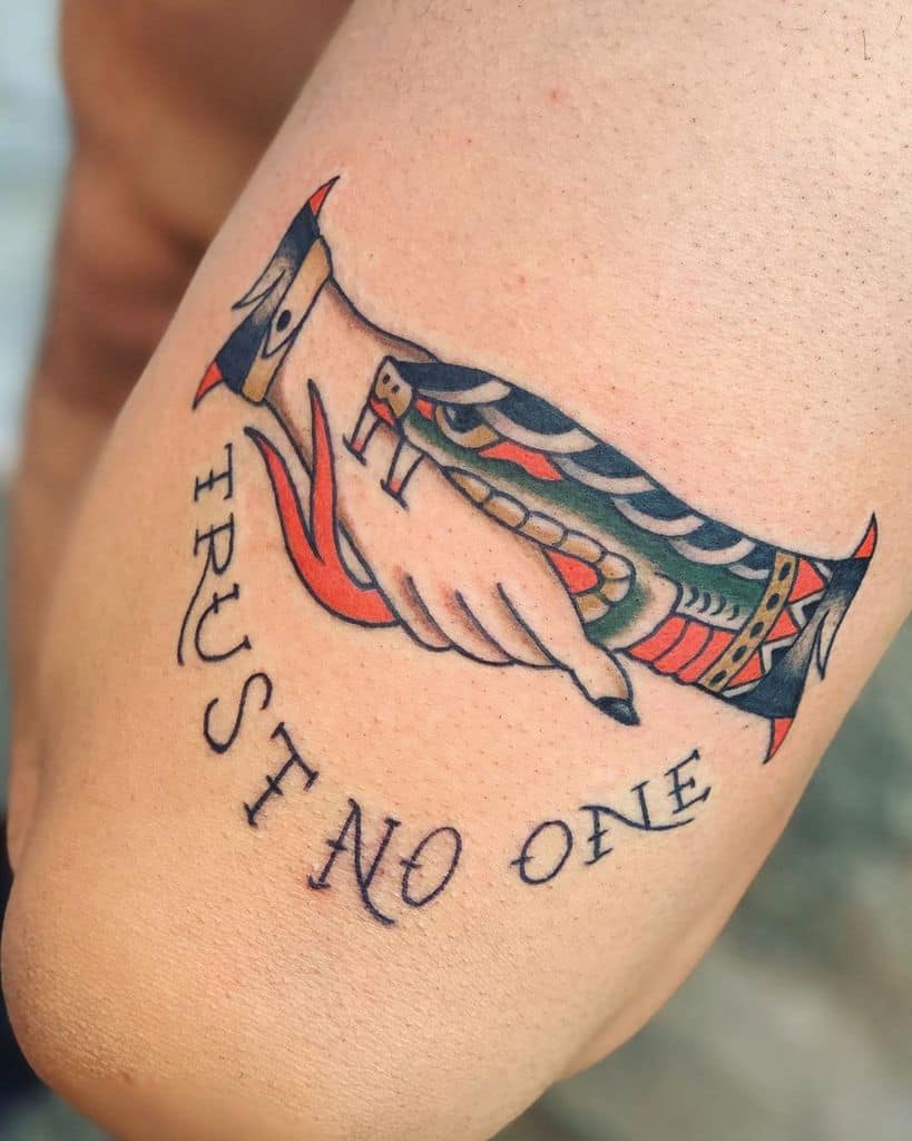 Traditional tattoo featuring a handshake with a serpent, bold lines, and intricate detailing. 'Trust No One' arches over the design, highlighting themes of caution and betrayal.