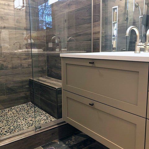 Rustic bathroom with wood paneling, glass shower, pebbled floor, and contemporary vanity