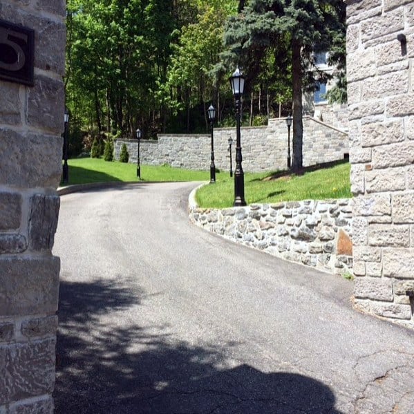 Driveway lined with vintage tall pole lights, adding a traditional and elegant touch to the path with greenery and stone walls on either side