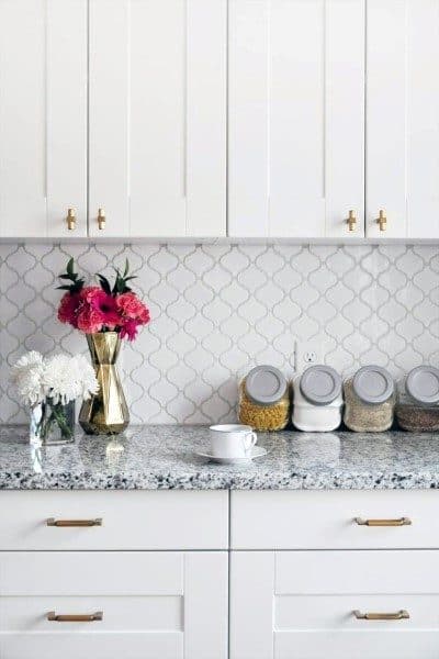 White kitchen with arabesque tile backsplash, granite countertop, and gold hardware accents.
