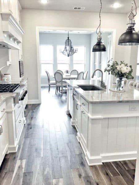 White kitchen with marble island, dark pendant lights, and hardwood flooring.