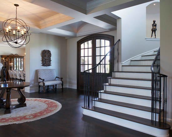 Spacious foyer with dark wood floors, a sweeping staircase, arched doors, and a modern chandelier