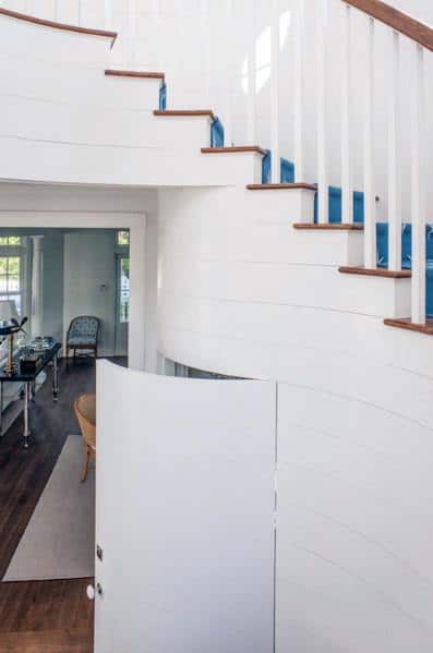 Curved white staircase with a hidden door under the stairs leading to additional storage space.