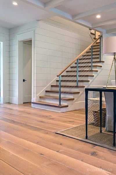 Open, modern staircase with cable railing in a bright room featuring wooden floors and a sleek table