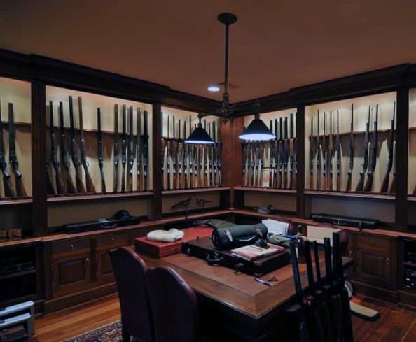 Classic gun room with warm wood paneling, built-in illuminated cabinets, and a central workspace for maintenance.