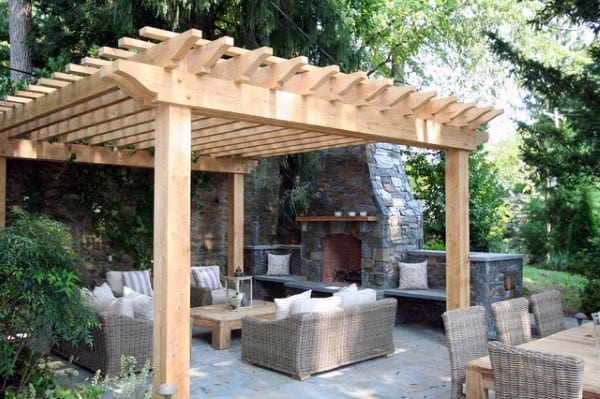 Charming wooden pergola with wicker seating, a rustic stone fireplace, and a serene outdoor setting.