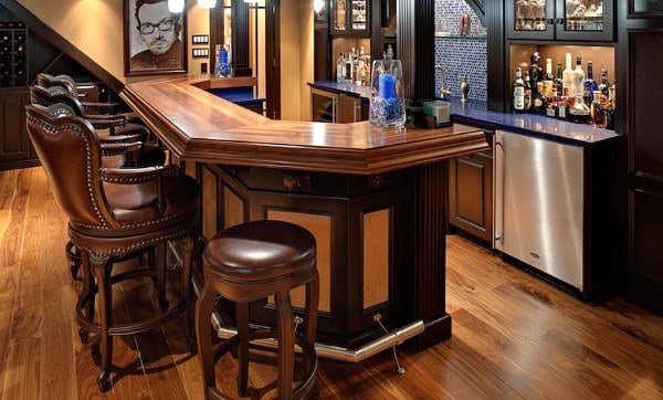 Traditional wood bar top with leather bar stools, hardwood flooring, and a fully stocked bar.