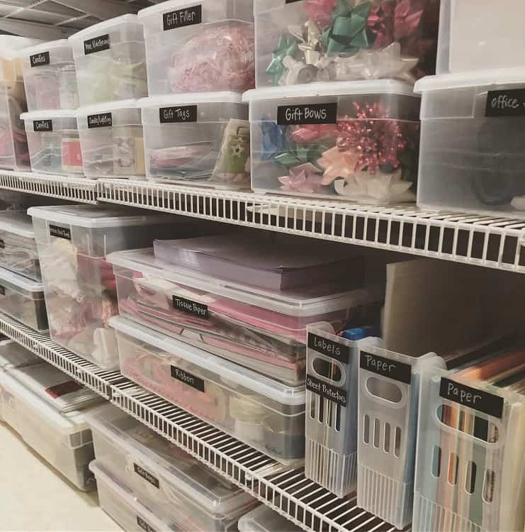 Basement shelves with labeled transparent bins for storing gift wrapping supplies and paper products.