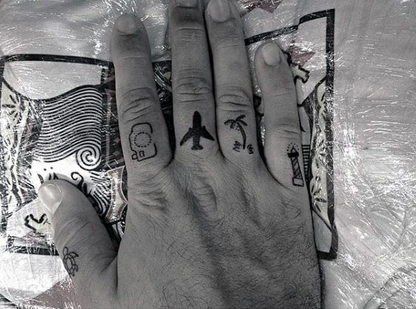 Hand with small tattoos on fingers including a plane, palm tree, and a lighthouse
