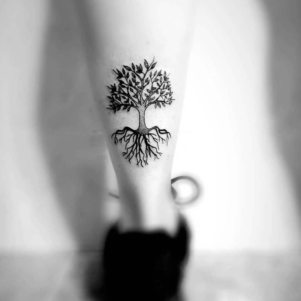 Minimalist tree tattoo on the calf, beautifully showcasing roots and branches in perfect harmony