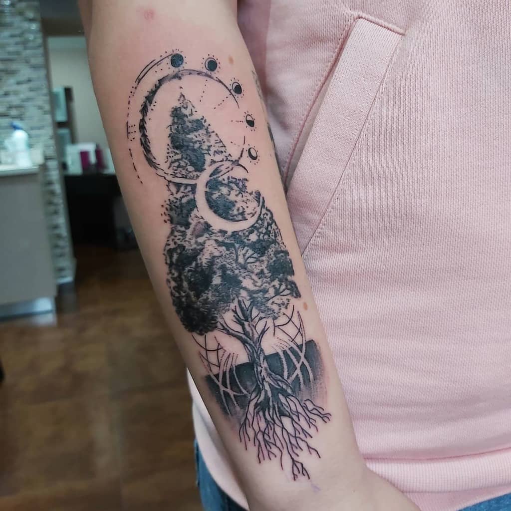 Forearm tattoo of a tree blending into cosmic elements, featuring moon phases and roots, symbolizing the connection between earth and the universe