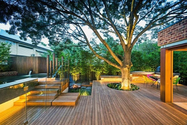 Spacious wooden deck with integrated tree, glass railing, small pool, and outdoor seating areas.