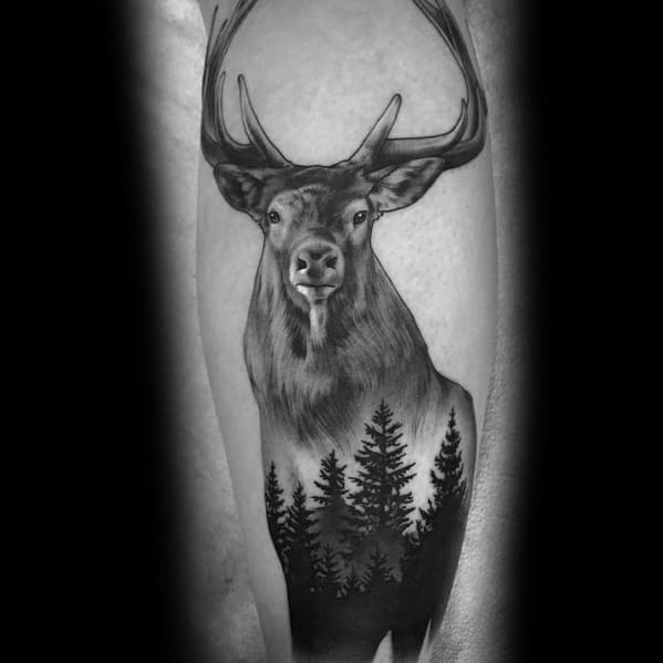 Realistic black and grey elk tattoo on the forearm, featuring bold antlers, fine shading, and a forest silhouette for a striking nature-inspired design.