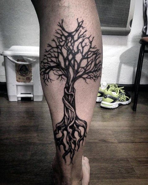 Black ink tree tattoo on the calf, featuring twisted roots and branches wrapping around the leg for a bold and organic nature-inspired design.
