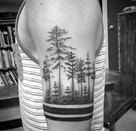 Black and grey upper arm tattoo of a dense pine forest with towering trees, complemented by bold armband lines for a striking contrast.