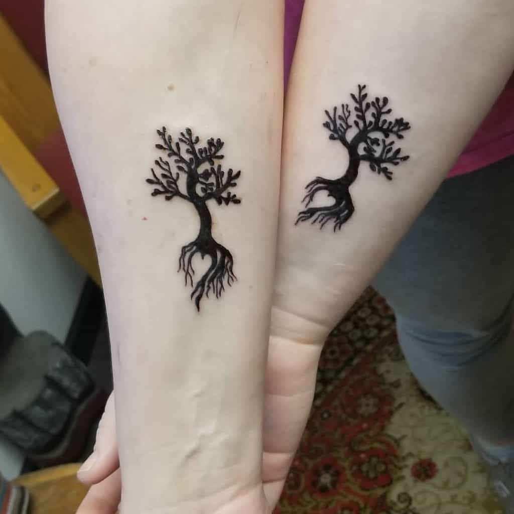 Matching mother-daughter tree tattoos in sihouette featuring twisting branches and roots