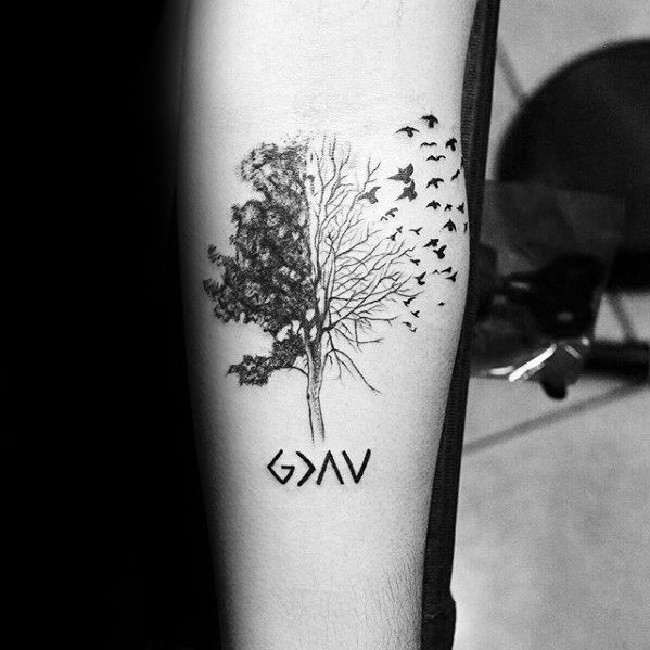 Forearm tattoo featuring "God is greater than the highs and lows" symbol with a detailed tree and flying birds design