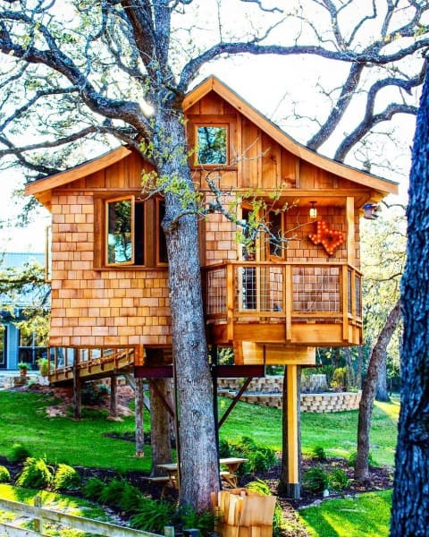 A wooden treehouse nestled among trees with a small balcony and lush greenery surrounding it