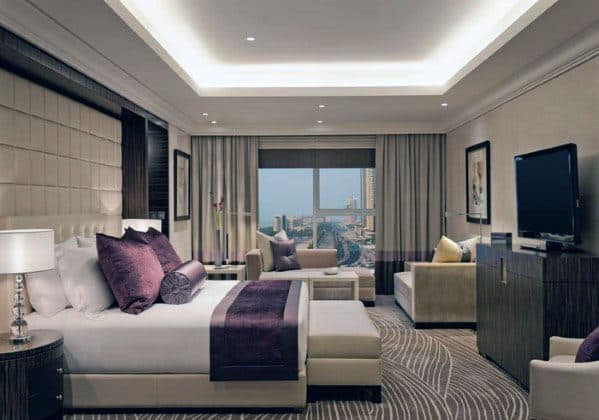 Contemporary bedroom with city view, neutral decor, and cozy seating area.