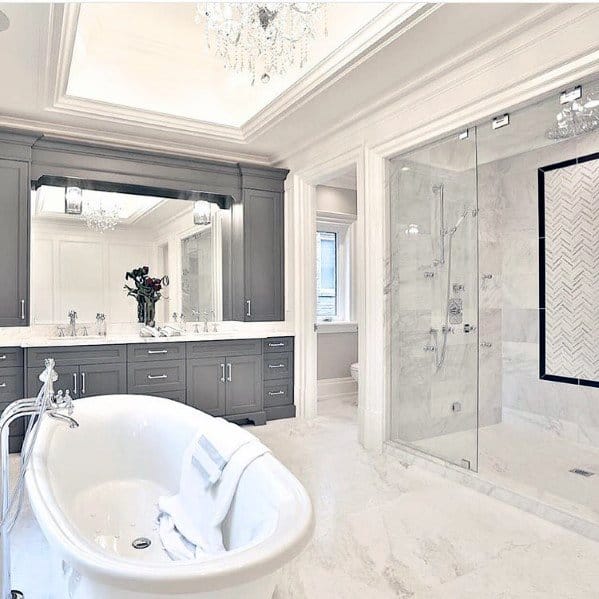 Elegant bathroom with freestanding tub, marble floors, glass shower, and recessed cove lighting with chandeliers.
