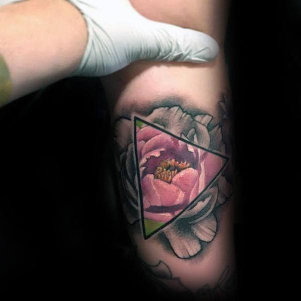Tattoo features a beautiful peony design encased within a triangle, creating a stunning color contrast and illusion effect on the inner arm