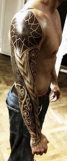 Man with an elaborate tribal tattoo sleeve on his left arm, standing shirtless