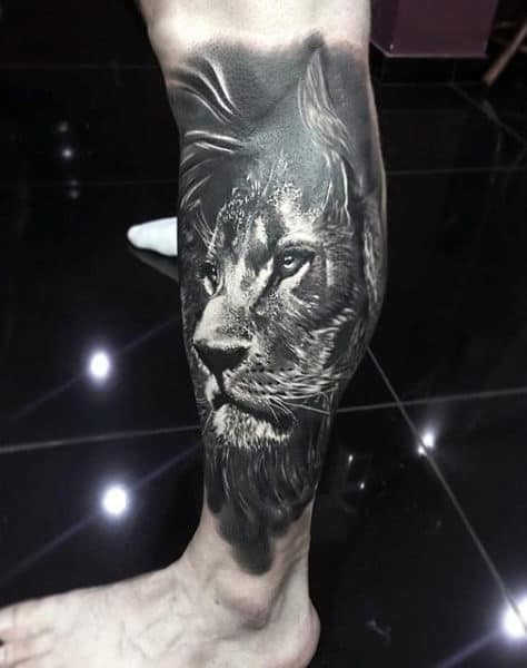 Realistic black and grey calf tattoo of a lion's face, with intricate shading and fine details for a bold and majestic look