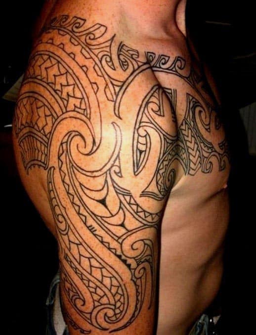 Upper body of a person with an intricate black tribal tattoo on their shoulder and chest