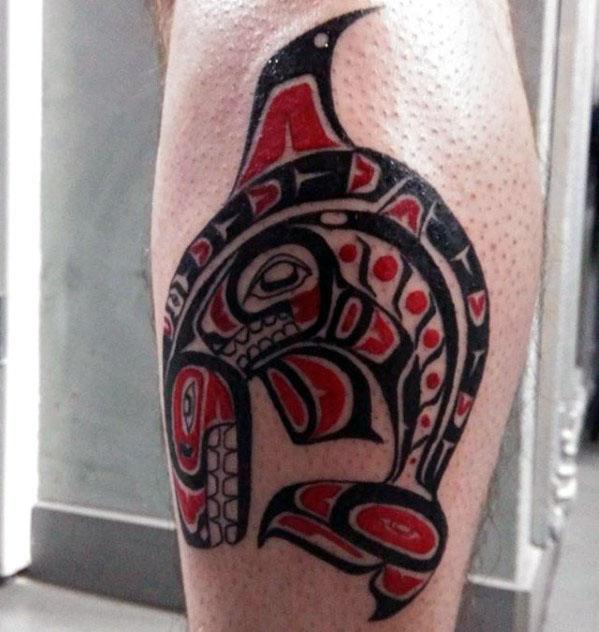 Bold tribal-style orca tattoo on the calf, featuring striking black and red patterns, with intricate detailing that forms the shape of the whale.