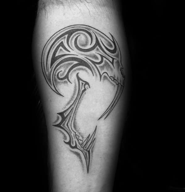 Stylized tribal skull tattoo with sharp curved lines and abstract detailing, forming a sleek and modern design on the calf.