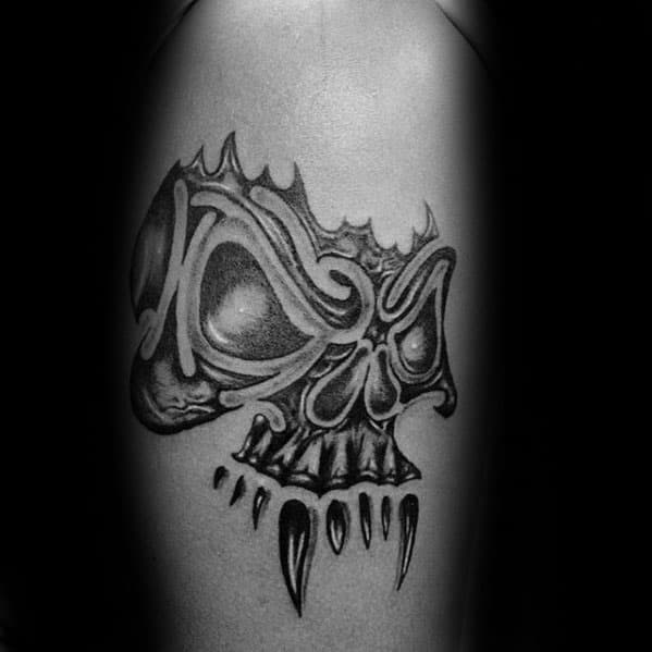 Abstract tribal skull tattoo with exaggerated features, bold curves, and pointed teeth for a surreal, aggressive design on the upper arm.