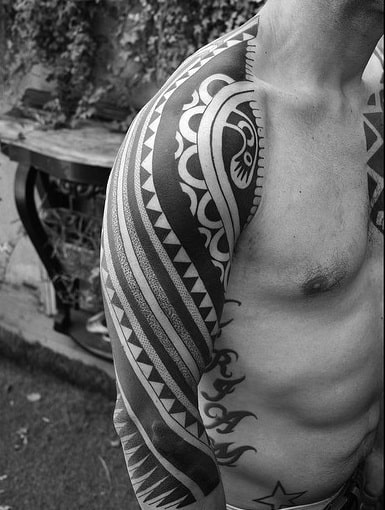 Black and white image of a man's intricate tribal shoulder and arm tattoos