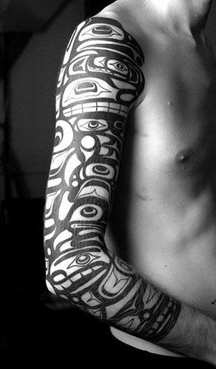 Person with a full-sleeve tribal tattoo on their left arm in black and white